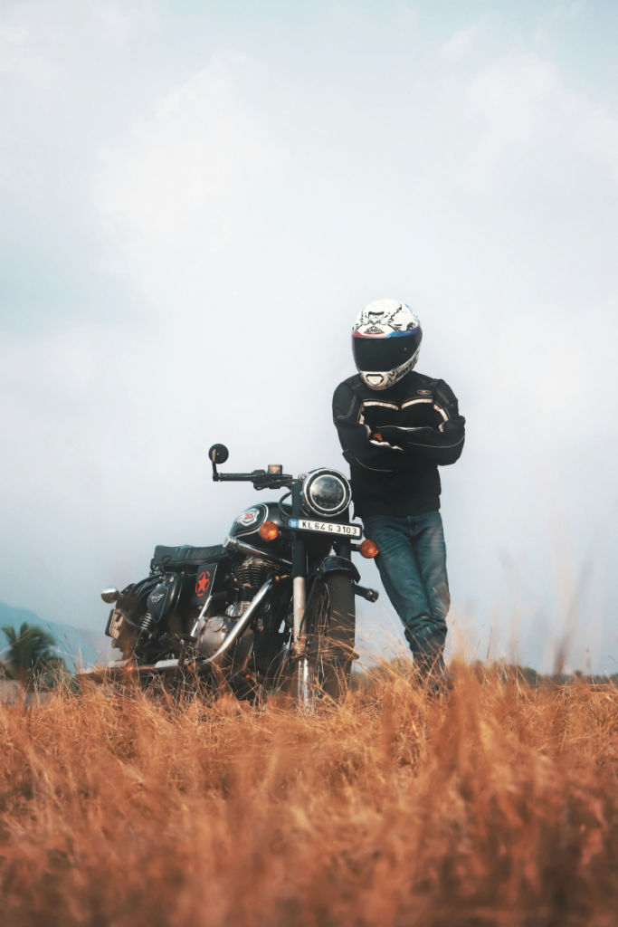 A fully geared motorcyclist stands confidently beside a classic bike in a golden field, embodying the freedom and responsibility of safe riding.