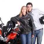 A smiling couple stands confidently next to their motorcycle, dressed in proper riding gear—highlighting the importance of motorcycle safety through preparation and protective clothing.