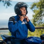 A motorcyclist fastens his motorcycle safety helmet while seated on a blue sport bike, emphasizing the importance of protective gear before riding.