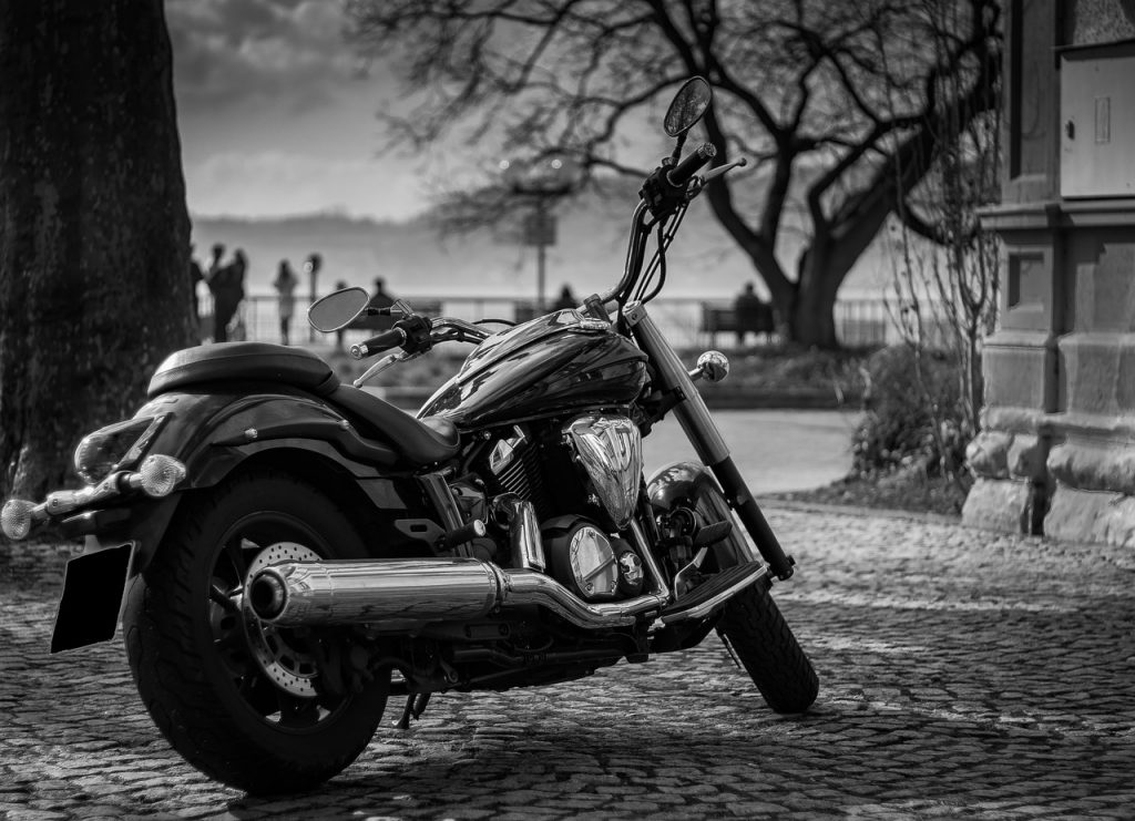 A sleek cruiser motorcycle is parked on a cobblestone path near a scenic lakeside, perfect for Montana motorcycle rides.