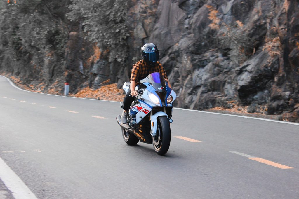 A motorcyclist in a plaid shirt and full-face helmet rides a sportbike along a winding mountain road.