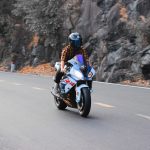 A motorcyclist in a plaid shirt and full-face helmet rides a sportbike along a winding mountain road.