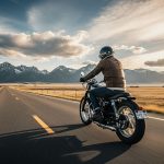 Man riding classic motorcycle on scenic Montana highway towards mountains at sunset