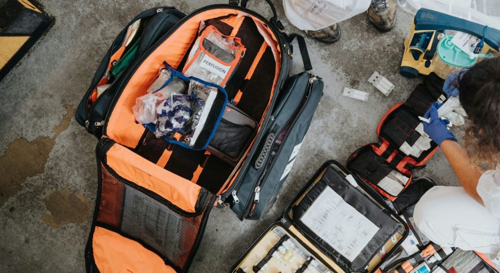 Open motorcycle emergency kit bag with organized medical supplies and tools spread out on the ground for roadside preparedness