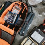 Open motorcycle emergency kit bag with organized medical supplies and tools spread out on the ground for roadside preparedness