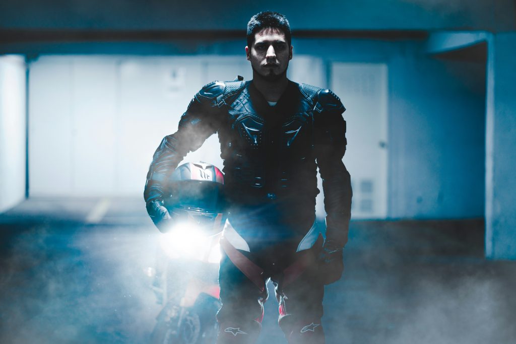 Motorcycle rider in full body armor standing with bike in a dimly lit garage