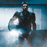 Motorcycle rider in full body armor standing with bike in a dimly lit garage