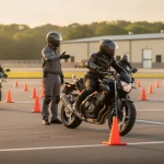 Motorcycle training exercise with riders navigating a cone slalom while an instructor signals from the center.